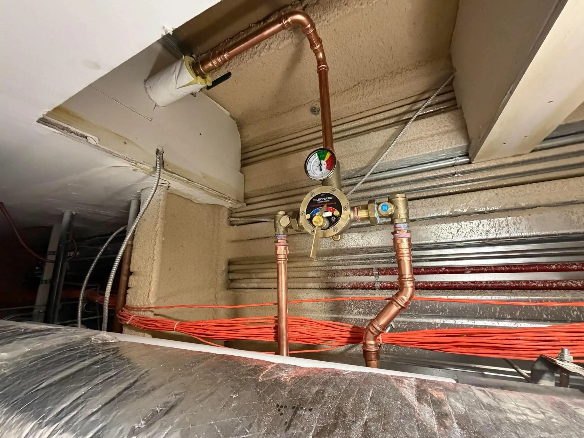 Mitigeur thermostatique installé dans un entre-plafond : tuyauterie de cuivre sertie, alignée entre les conduits de ventilation et le câblage